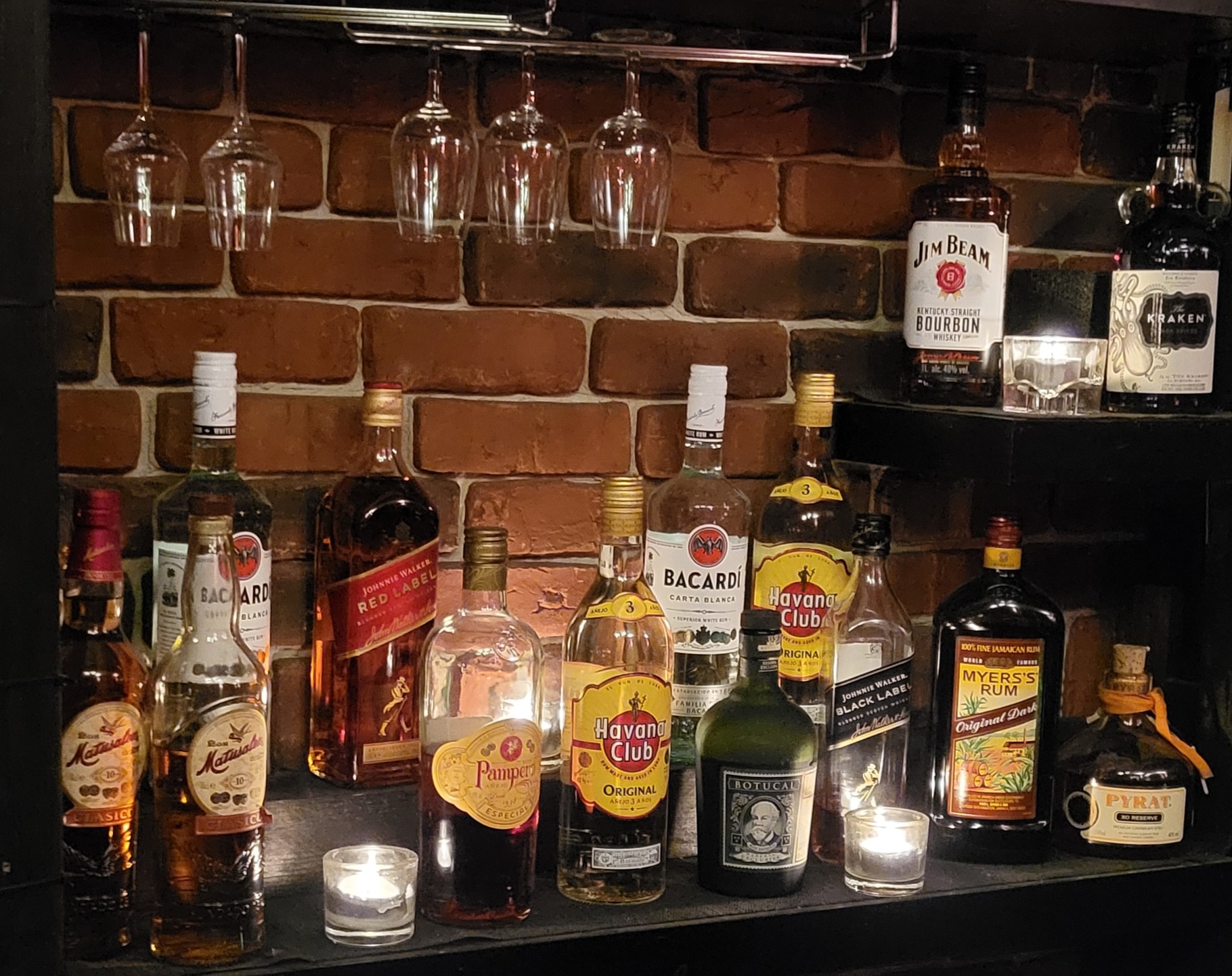 Rumflaschen an Backsteinwand mit Kerzen und Gläsern